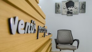 Una recepción con mostrador de madera y una silla frente a él. Se observan obras de arte enmarcadas en la pared detrás del mostrador.