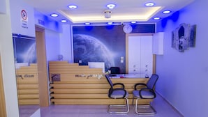 Zona de recepción con un escritorio de madera, dos sillas, un reloj y un mural en la pared.