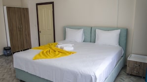Una cama bien tendida con sábanas blancas y una toalla amarilla, un armario de madera y una mesita de noche con cajones.