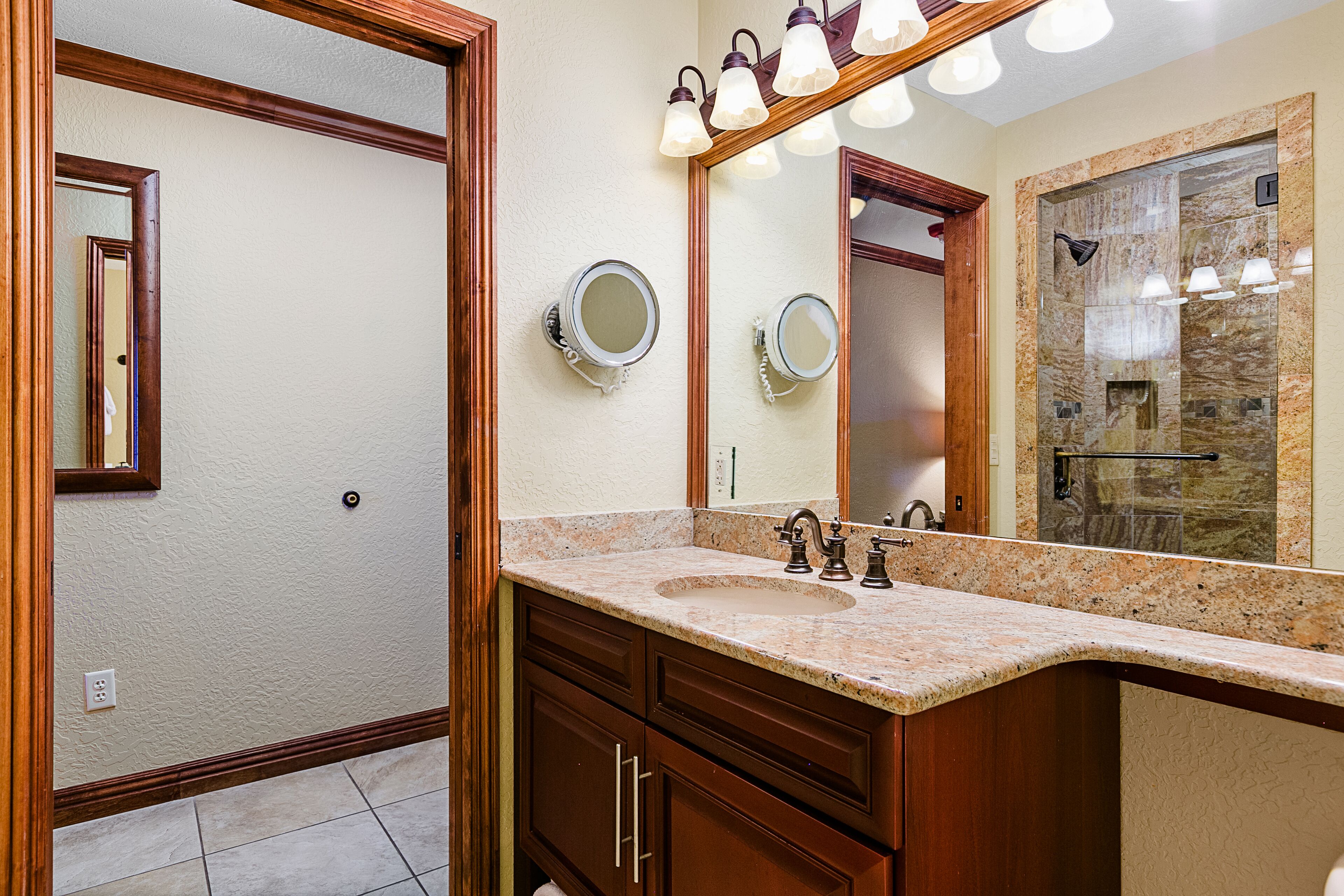 A bathroom with a granite countertop, a sink, a mirror, and a shower area.