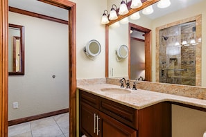 Een badkamer met een granieten aanrechtblad, een wastafel, een spiegel en een douche.