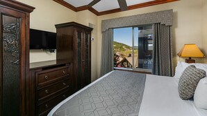 Une chambre d’hôtel avec un grand lit, un ventilateur de plafond, une télévision, une commode et une fenêtre donnant sur une colline.