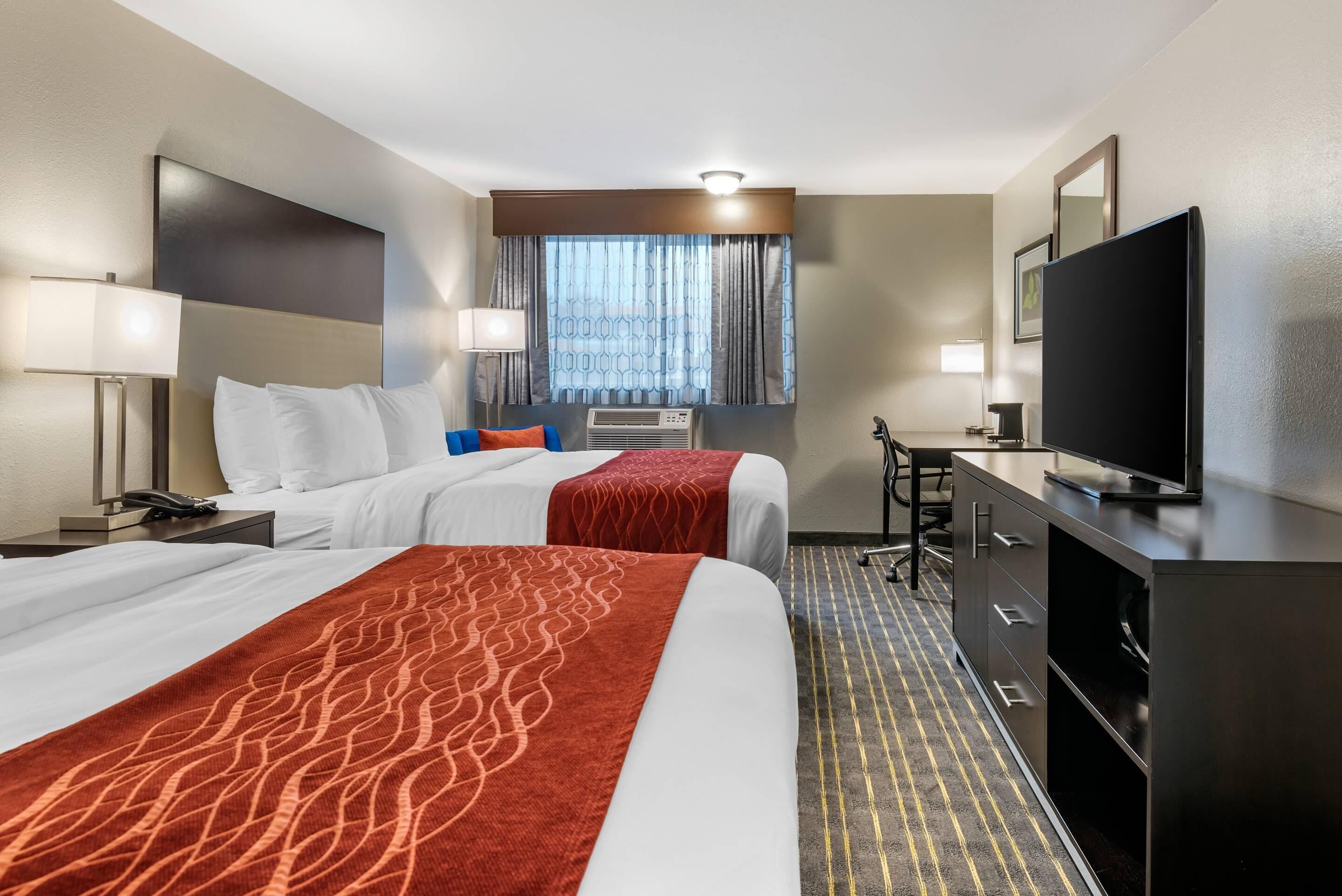 Une chambre d’hôtel avec deux lits, un bureau, une télévision et une fenêtre avec des rideaux.