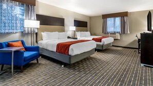 A hotel room with two beds, a blue armchair, a desk, and a dresser. - Comfort Inn & Suites Tigard near Washington Square (Tigard)