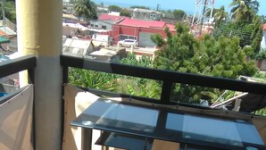 Een balkon met een metalen tafel en stoelen, stenen vloertegels en uitzicht op gebouwen en palmbomen.