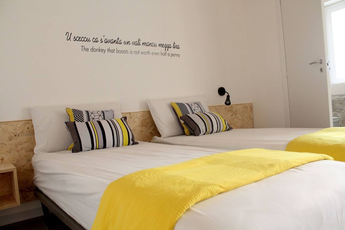 A hotel room with two beds, a wooden headboard, and a wall quote in a foreign language.