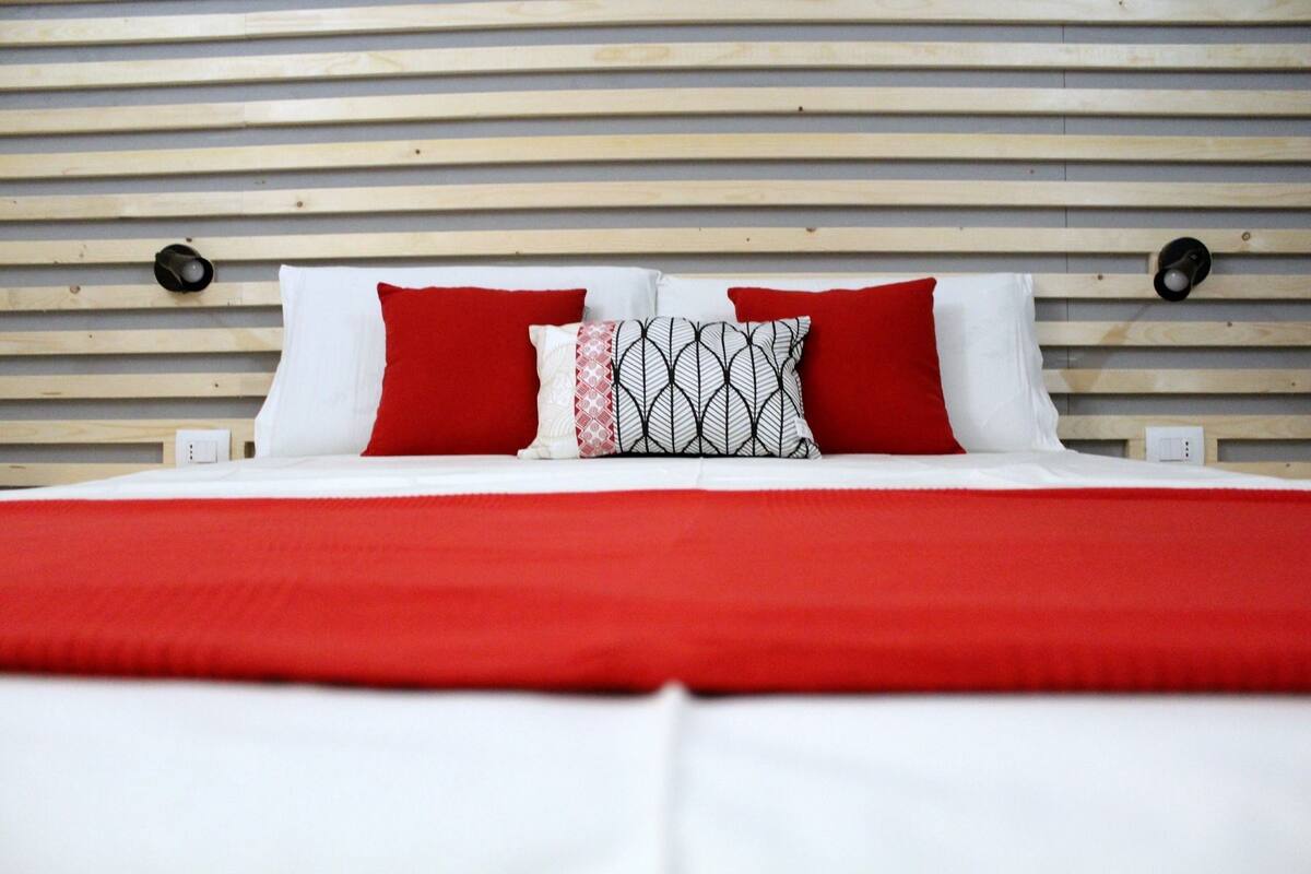 A bed with a red and white bedspread, two red pillows, and a patterned pillow.