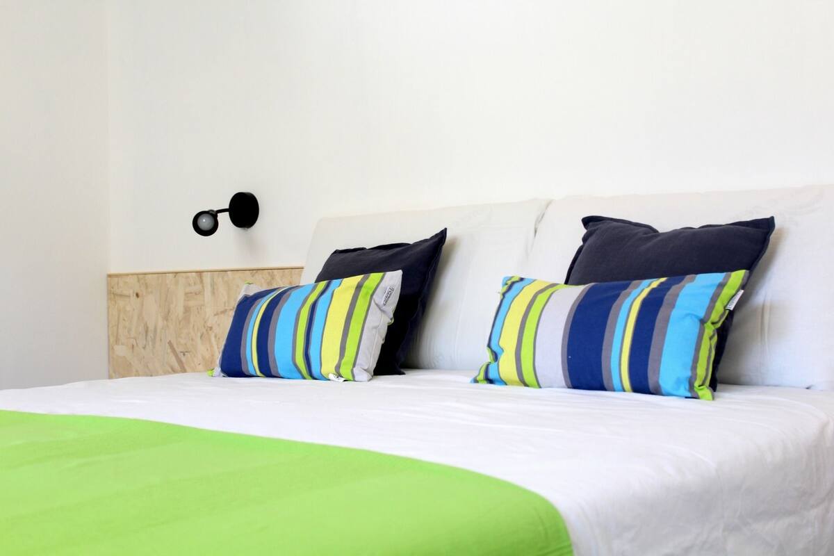 A bed with a green blanket, two striped pillows, and a wooden headboard.