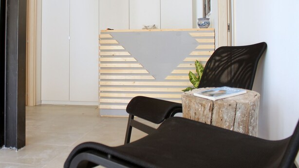 A modern interior with a wooden ceiling, a reception desk with a slanted design, and a black chair with a magazine on a wooden stump.