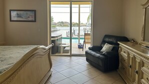 A bedroom with a bed, a chair, a vanity, and a view of a pool and outdoor area. - Beautiful Water Views, 5-min Walk to South Beach, Heated Pool, Hot Tub, 5 Bikes (Marco Island)