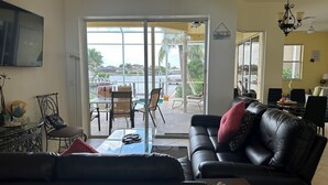 A living room with a black leather sofa, a glass coffee table, and a dining area with chairs and a table. - Beautiful Water Views, 5-min Walk to South Beach, Heated Pool, Hot Tub, 5 Bikes (Marco Island)
