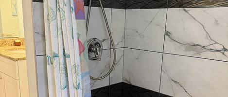 A shower with a handheld showerhead, a curtain with a fish pattern, and hexagonal tiles on the floor.