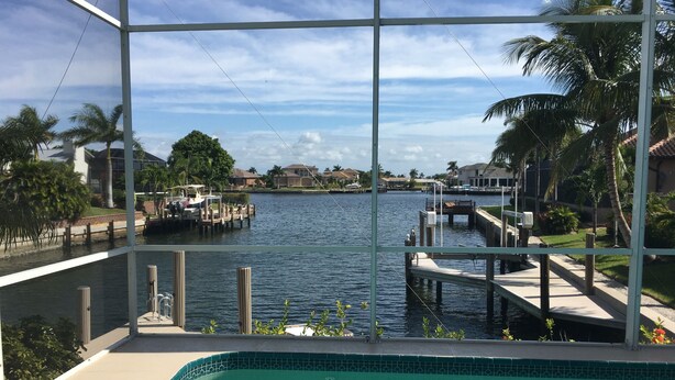 A view from a poolside area overlooking a marina with boats docked, surrounded by palm trees and residential buildings. - Beautiful Water Views, 5-min Walk to South Beach, Heated Pool, Hot Tub, 5 Bikes (Marco Island)