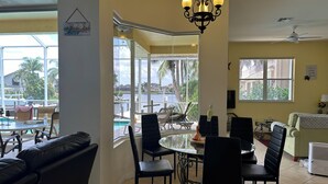 A dining area with a view of the pool and palm trees, a chandelier, and a ceiling fan. - Beautiful Water Views, 5-min Walk to South Beach, Heated Pool, Hot Tub, 5 Bikes (Marco Island)