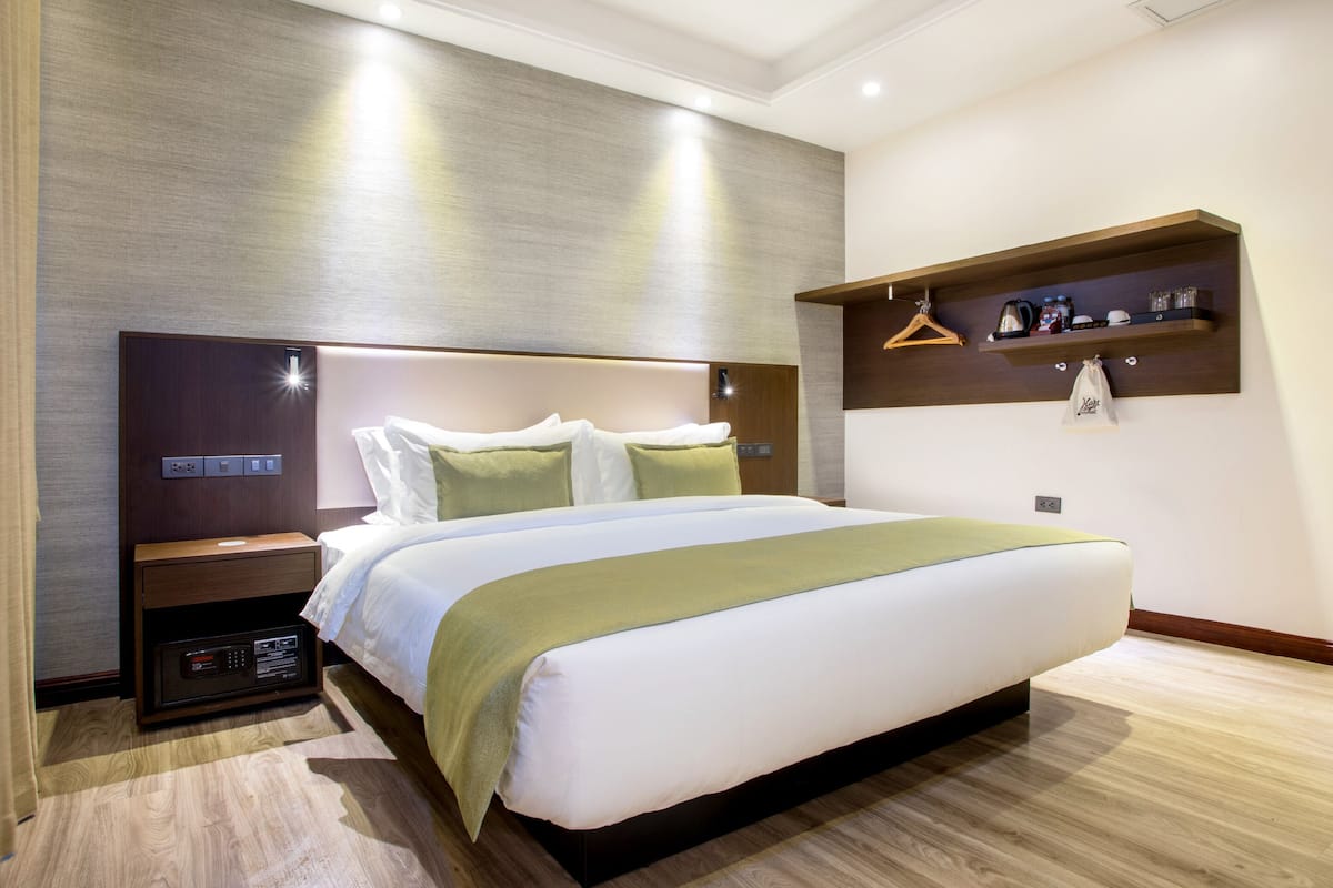Una habitación de hotel moderna con una cama grande, una mesita de noche con radio, un estante en la pared con artículos de tocador y suelo de madera.