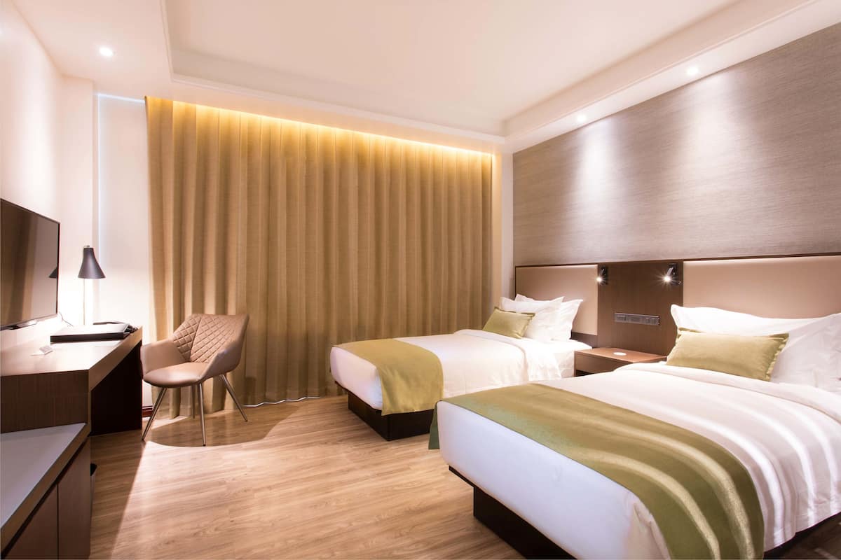 Habitación de hotel con dos camas, un escritorio, una silla y un ventanal con cortinas.