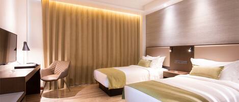 A hotel room with two beds, a desk, a chair, and a large window with curtains.