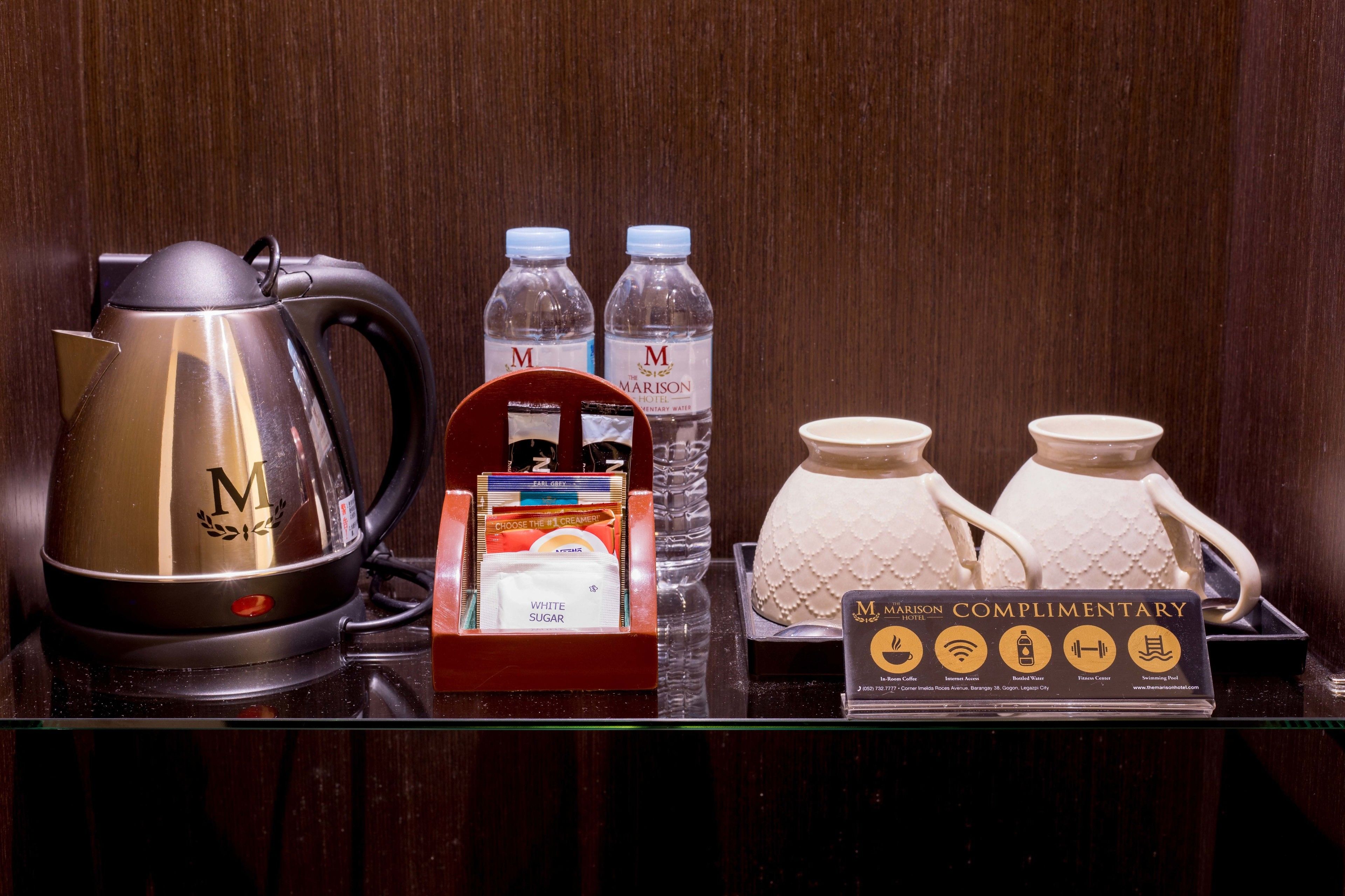 A hotel minibar setup with a coffee maker, bottled water, sugar packets, and a complimentary card.