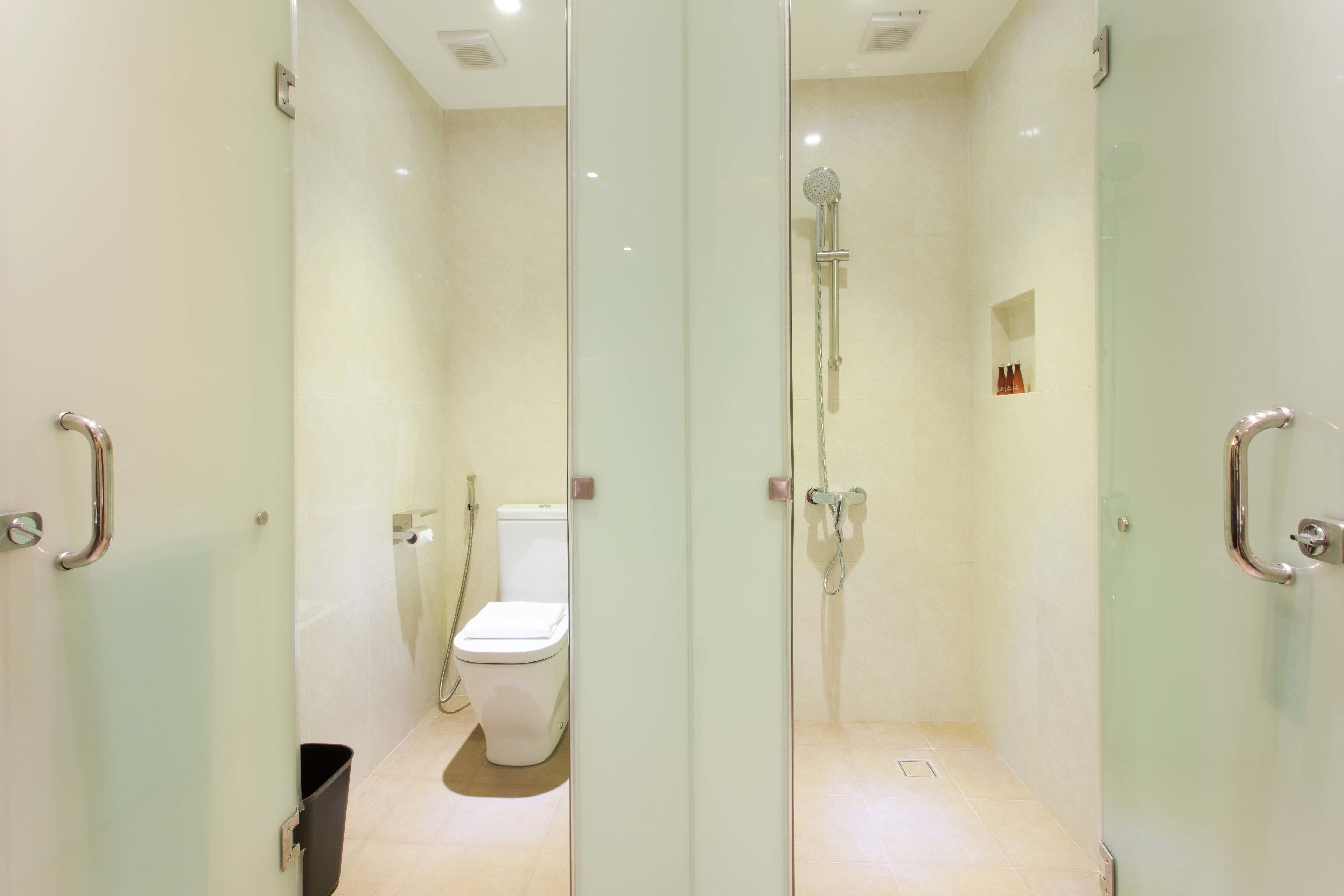 Um banheiro moderno com divisória de vidro, vaso sanitário, área de chuveiro e um pequeno nicho com produtos de higiene pessoal.