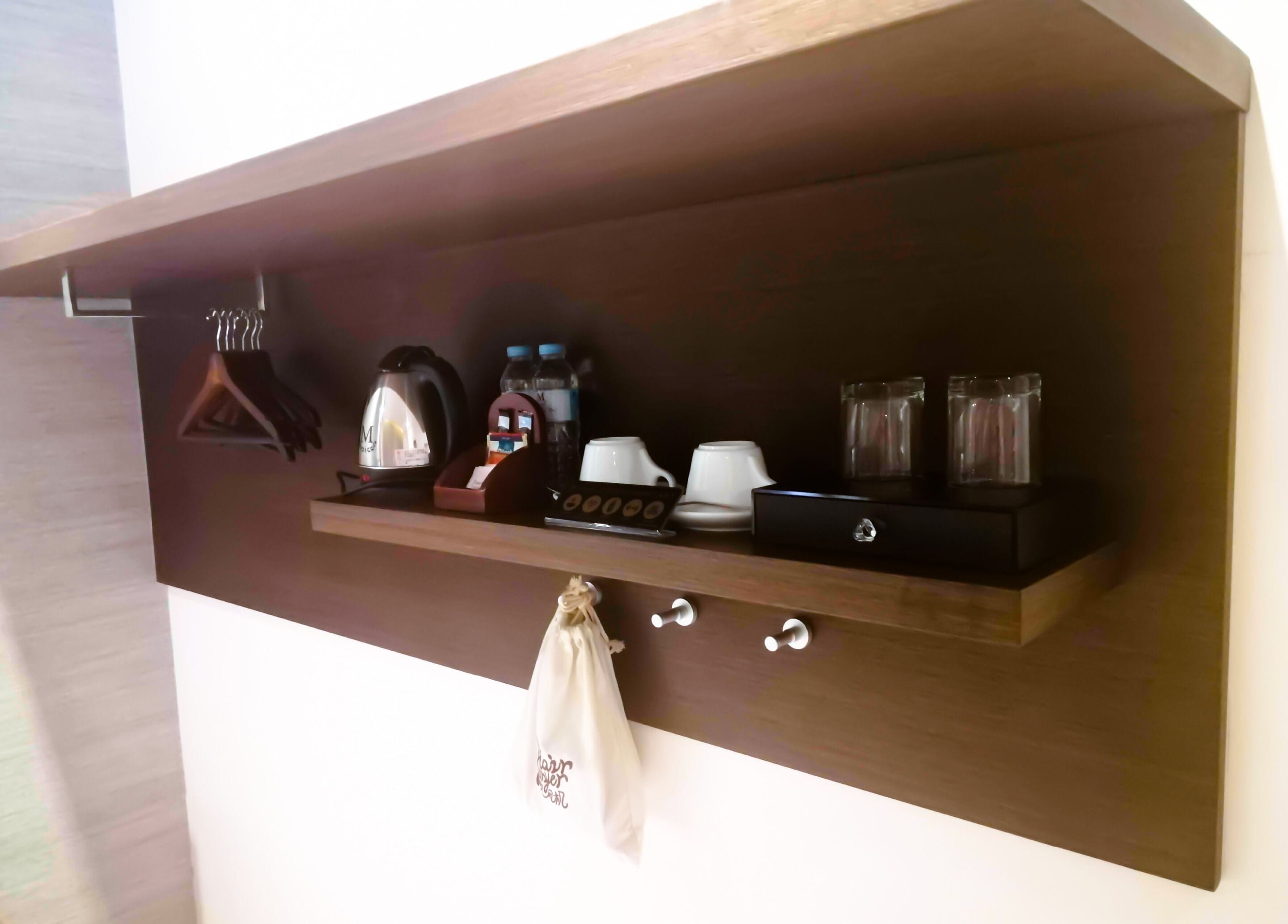 A dark wooden shelf with various items including a kettle, cups, a small clock, and a hanging bag.