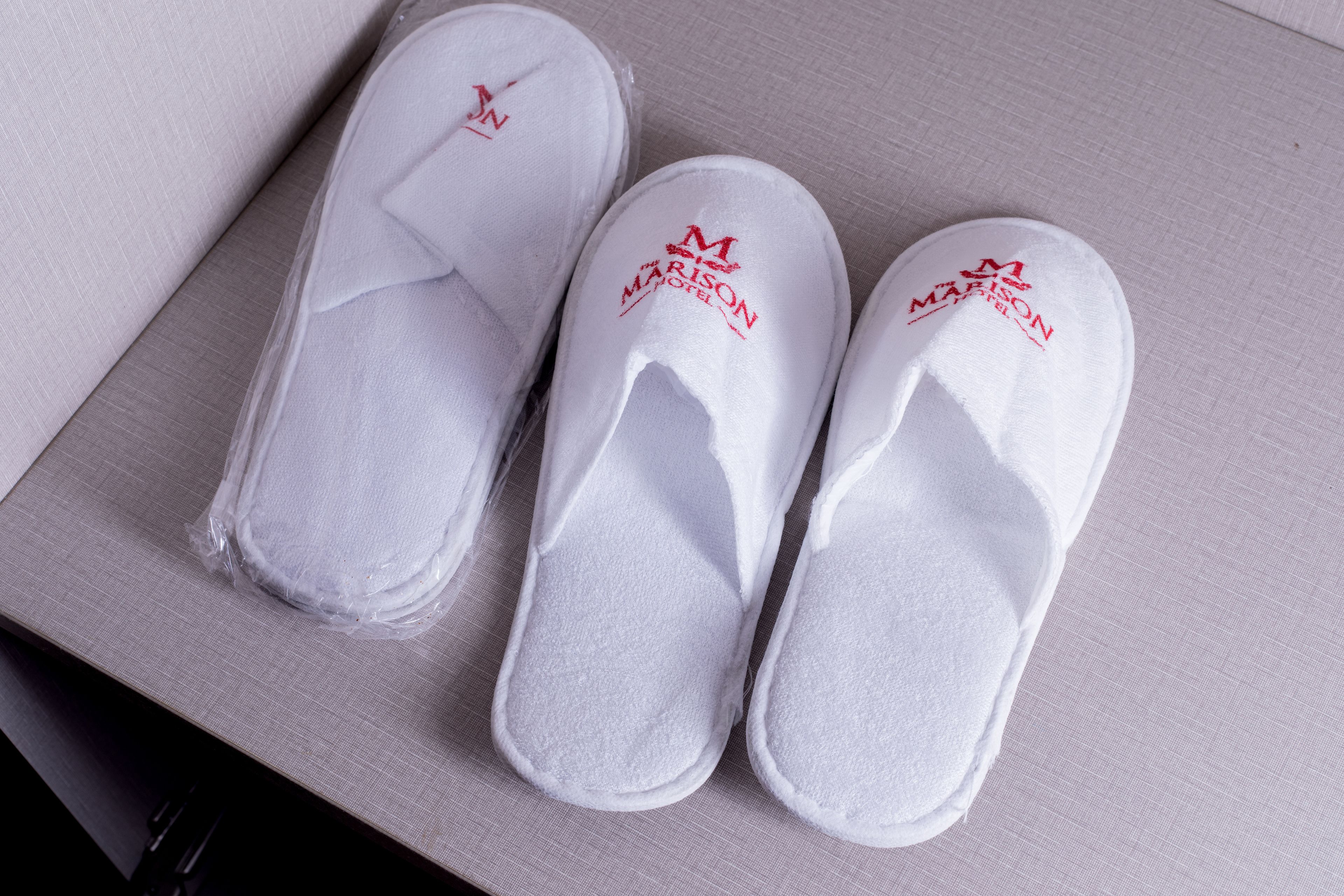A pair of white slippers with red text on the sole, placed on a textured surface.