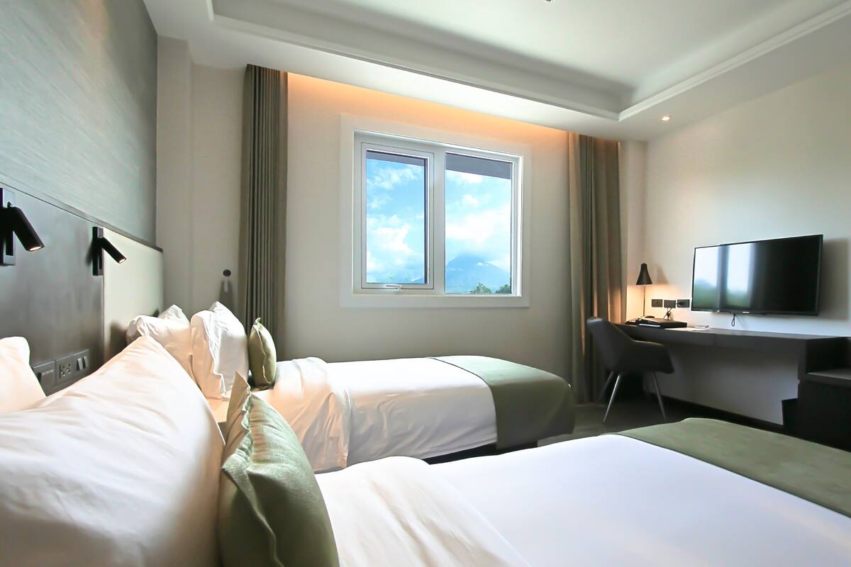 Habitación de hotel con dos camas, un escritorio, un televisor y una ventana con vista al cielo.