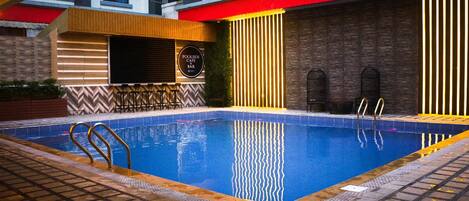 Une piscine dotée d’un bar, d’un espace détente au bord de la piscine et offrant une vue sur la façade du bâtiment.