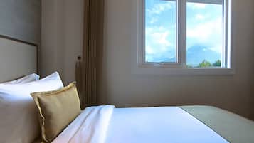 A hotel room with two beds, a window with a view of the sky and mountains, and a door with a curtain.