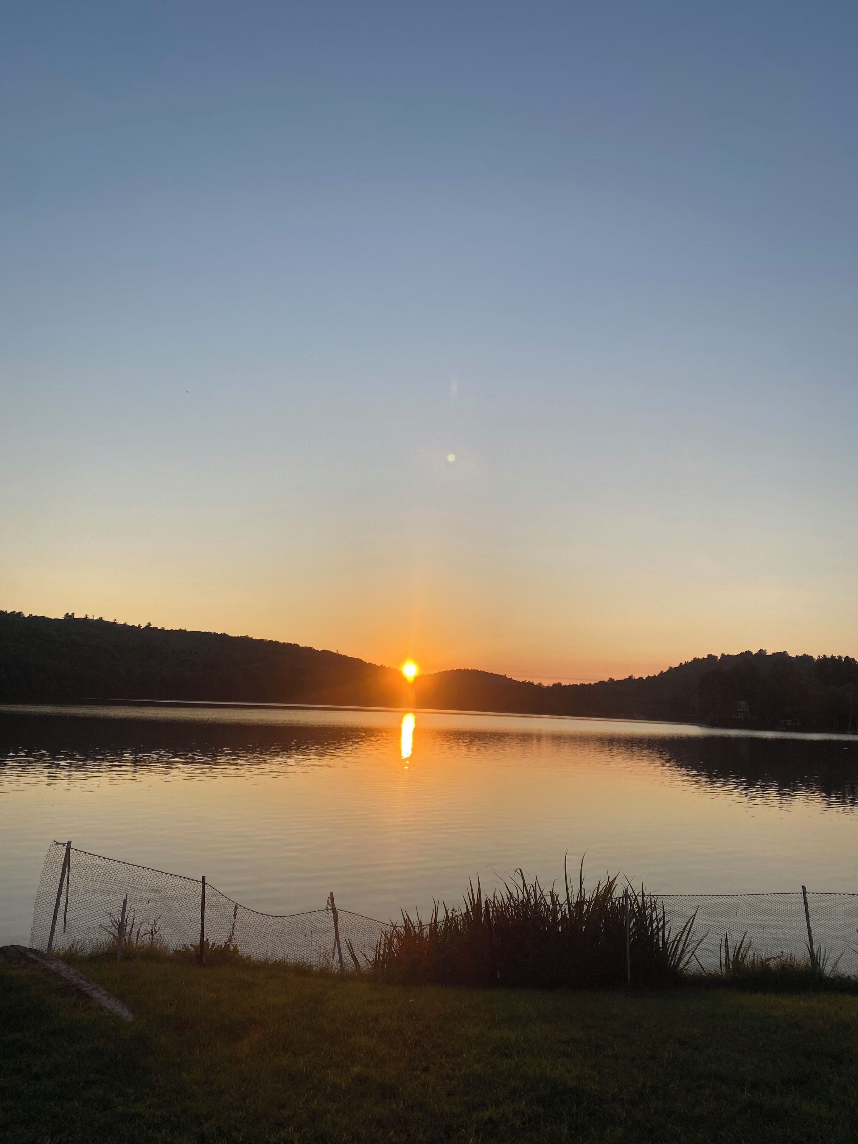 Un lac paisible au coucher du soleil, avec une clôture au premier plan.