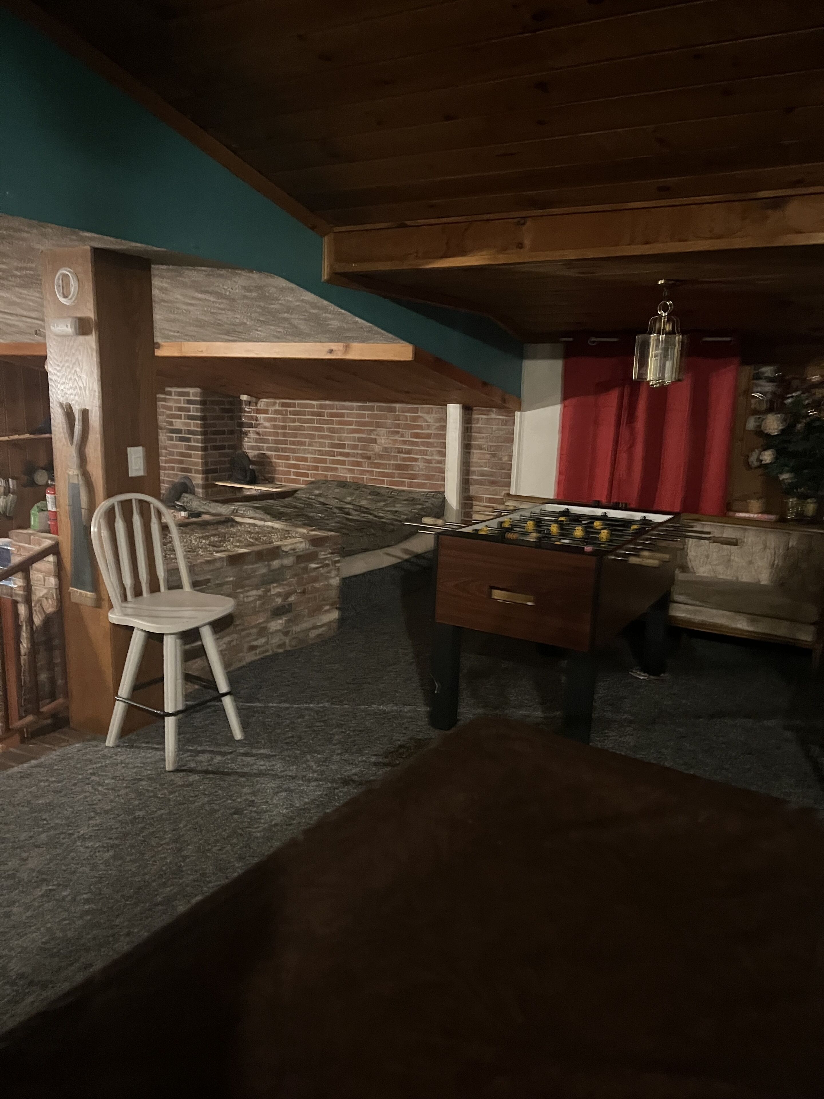 Une pièce chaleureuse avec une cheminée en briques, un plafond en bois et une table de baby-foot.