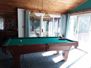 Una mesa de billar en una habitación con techo de madera y ventanas amplias.