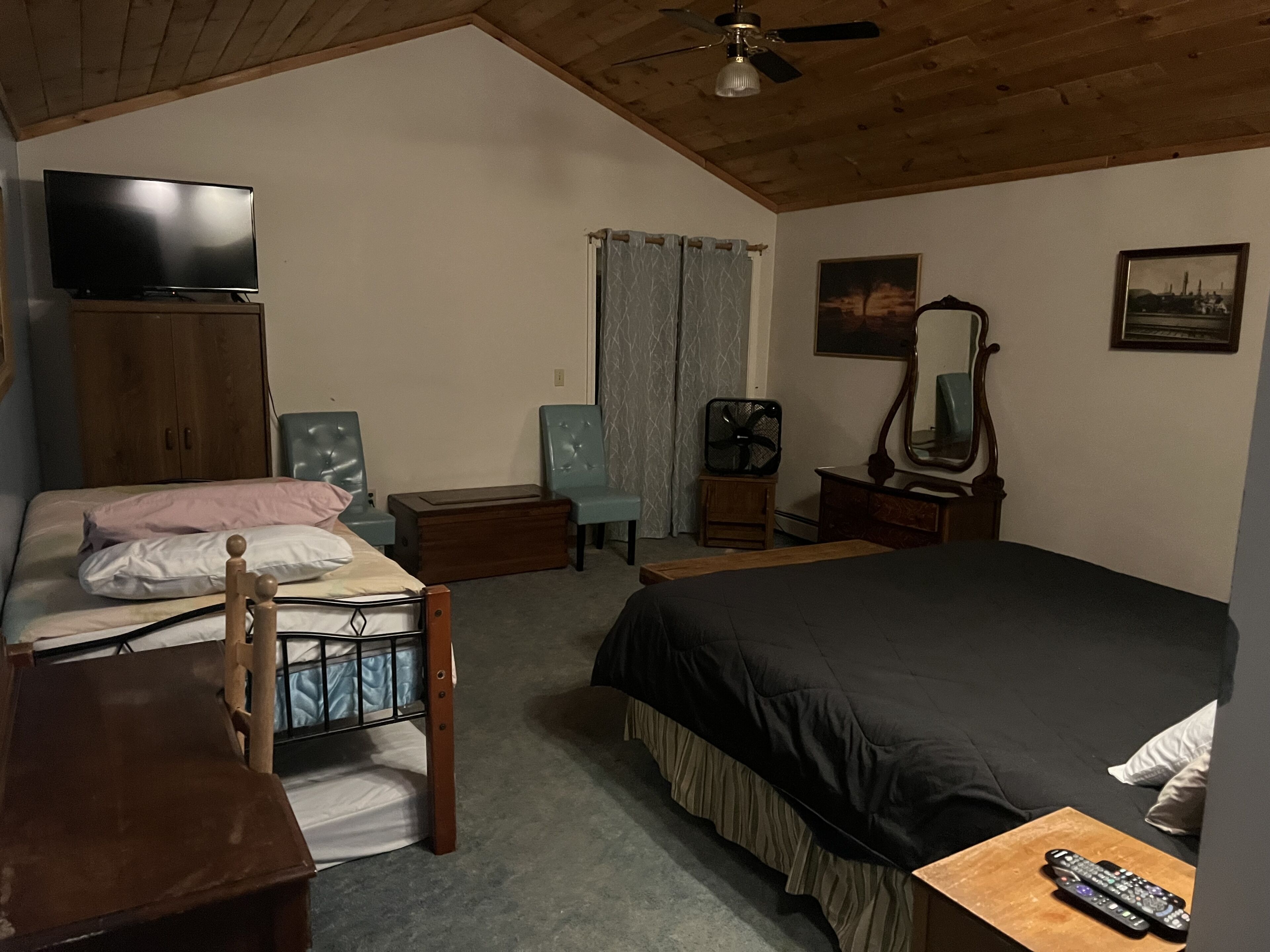 Ein Schlafzimmer mit Bett, Schreibtisch, Stuhl, Kommode, Fernseher, Ventilator und Spiegel.