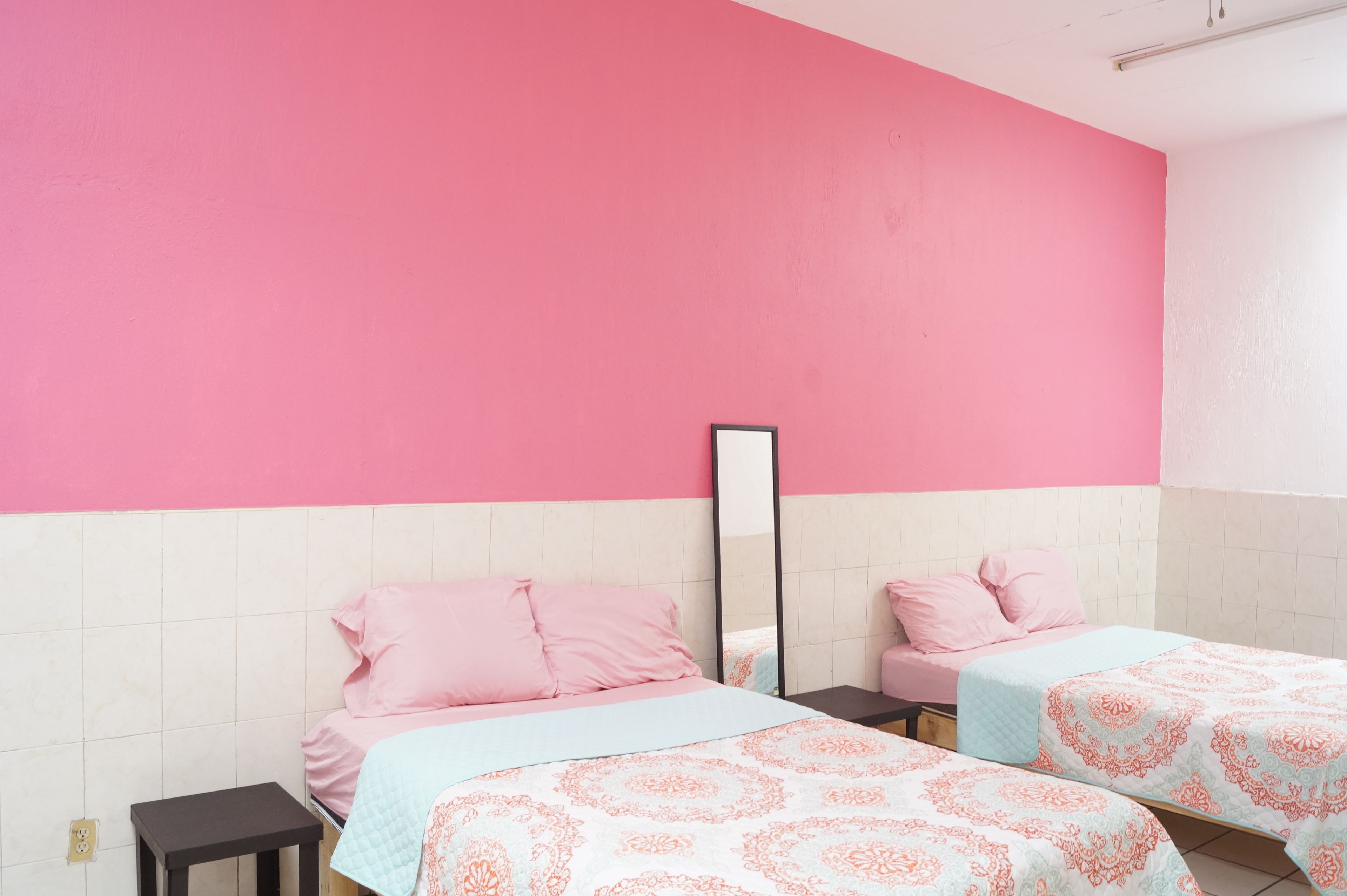 Una habitación con dos camas, cada una con ropa de cama rosa y edredón estampado. Hay una mesita pequeña y un espejo en la pared.