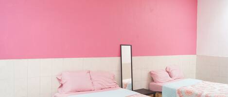 Una habitación con dos camas, cada una con ropa de cama rosa y edredón estampado. Hay una mesita pequeña y un espejo en la pared.
