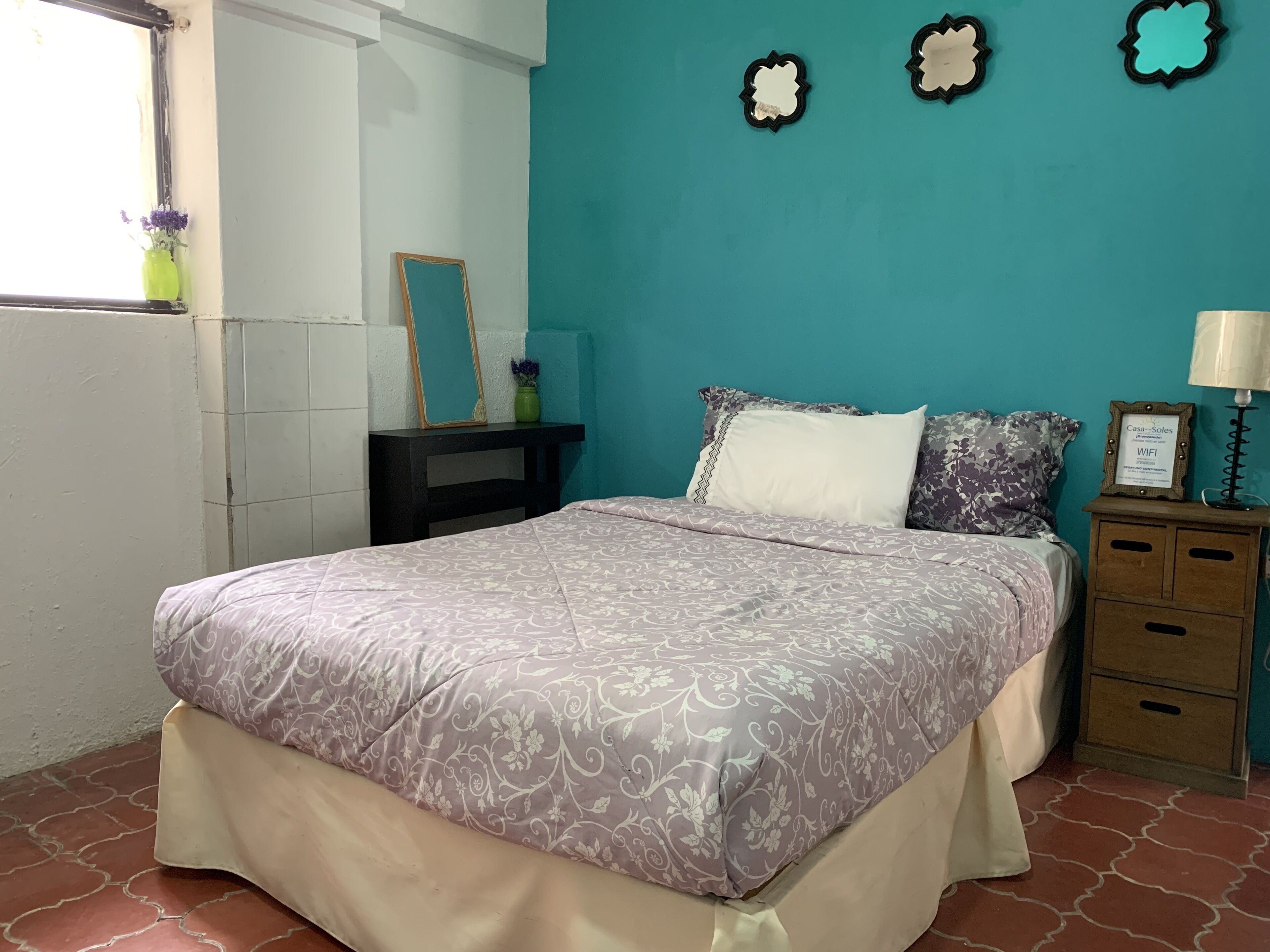 Un dormitorio con cama, mesita de noche, cómoda, espejo y pared decorada.