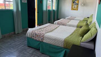 Ein Hotelzimmer mit zwei Betten, türkisfarbenen Wänden, einem Fenster mit Vorhängen, einer Wanduhr und einem Ventilator.