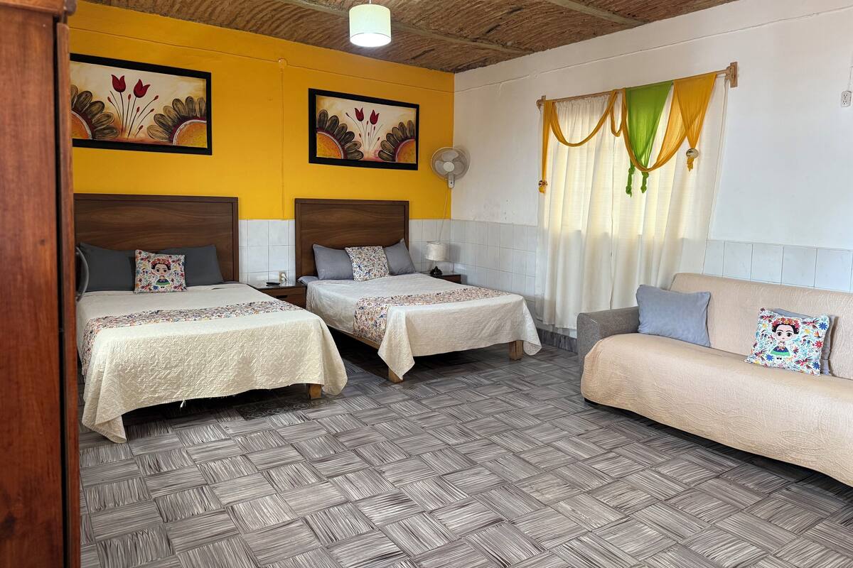 A hotel room with two beds, a sofa, a fan, and a window with curtains.