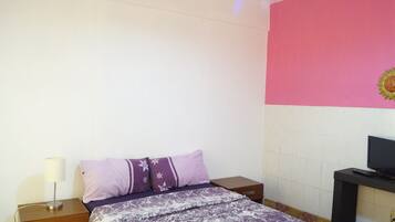 Un dormitorio con cama, mesita de noche, lámpara, televisión y un muro decorado con un motivo solar.
