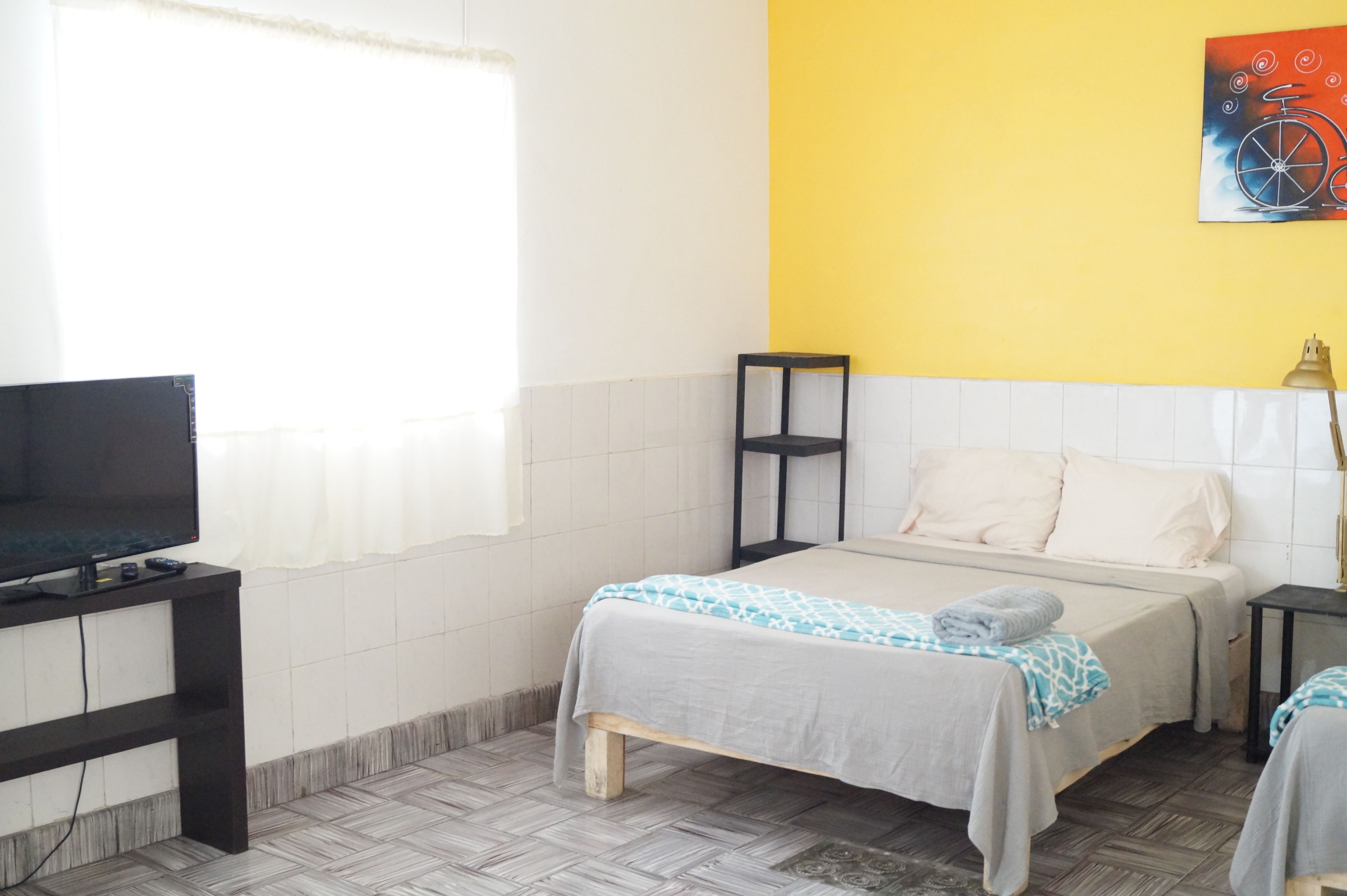 A hotel room with a bed, a TV, a small table, and a painting on the wall.