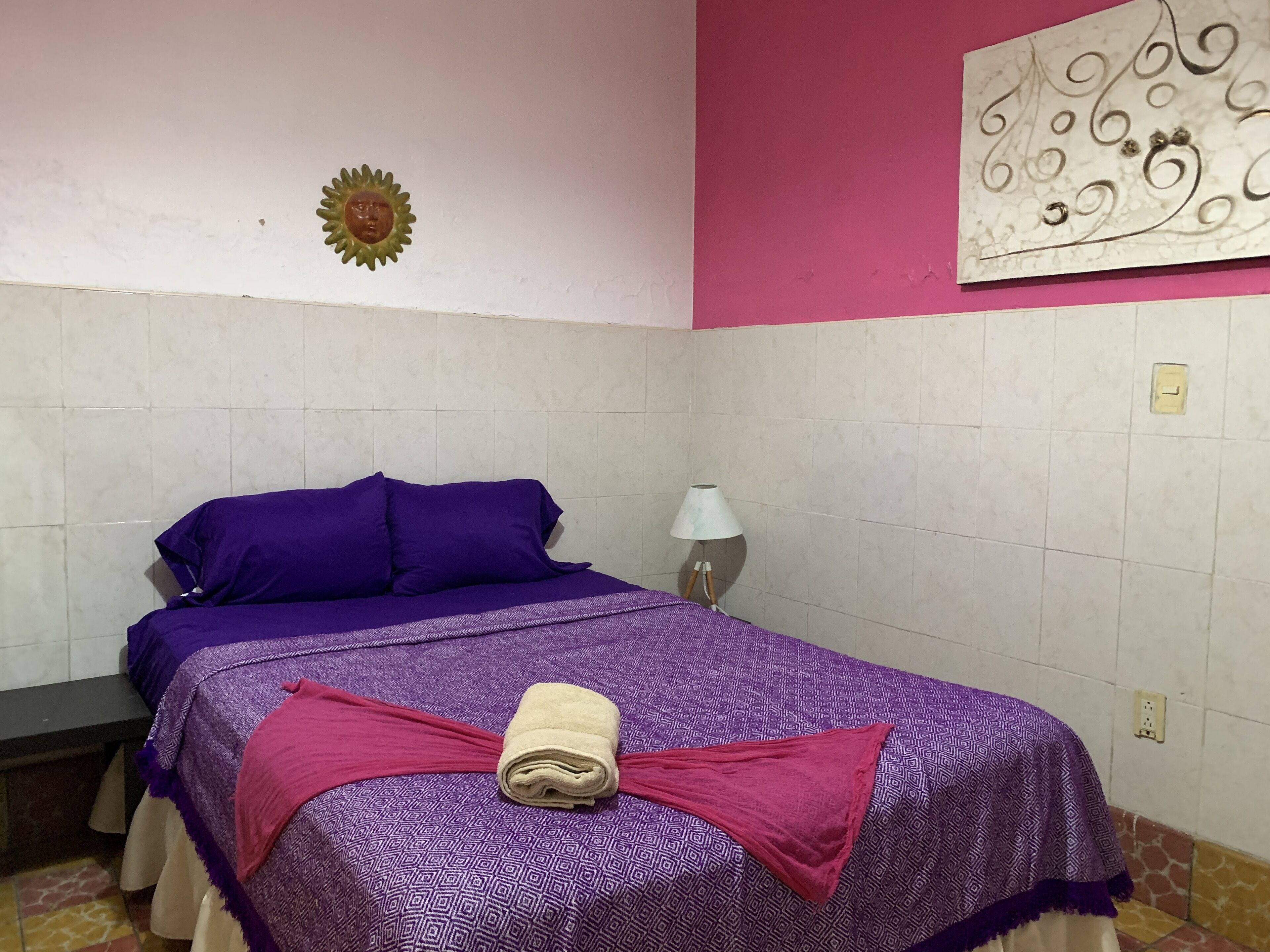 Una habitación con una cama, un reloj de pared, un adorno con forma de sol y una obra de arte en la pared.