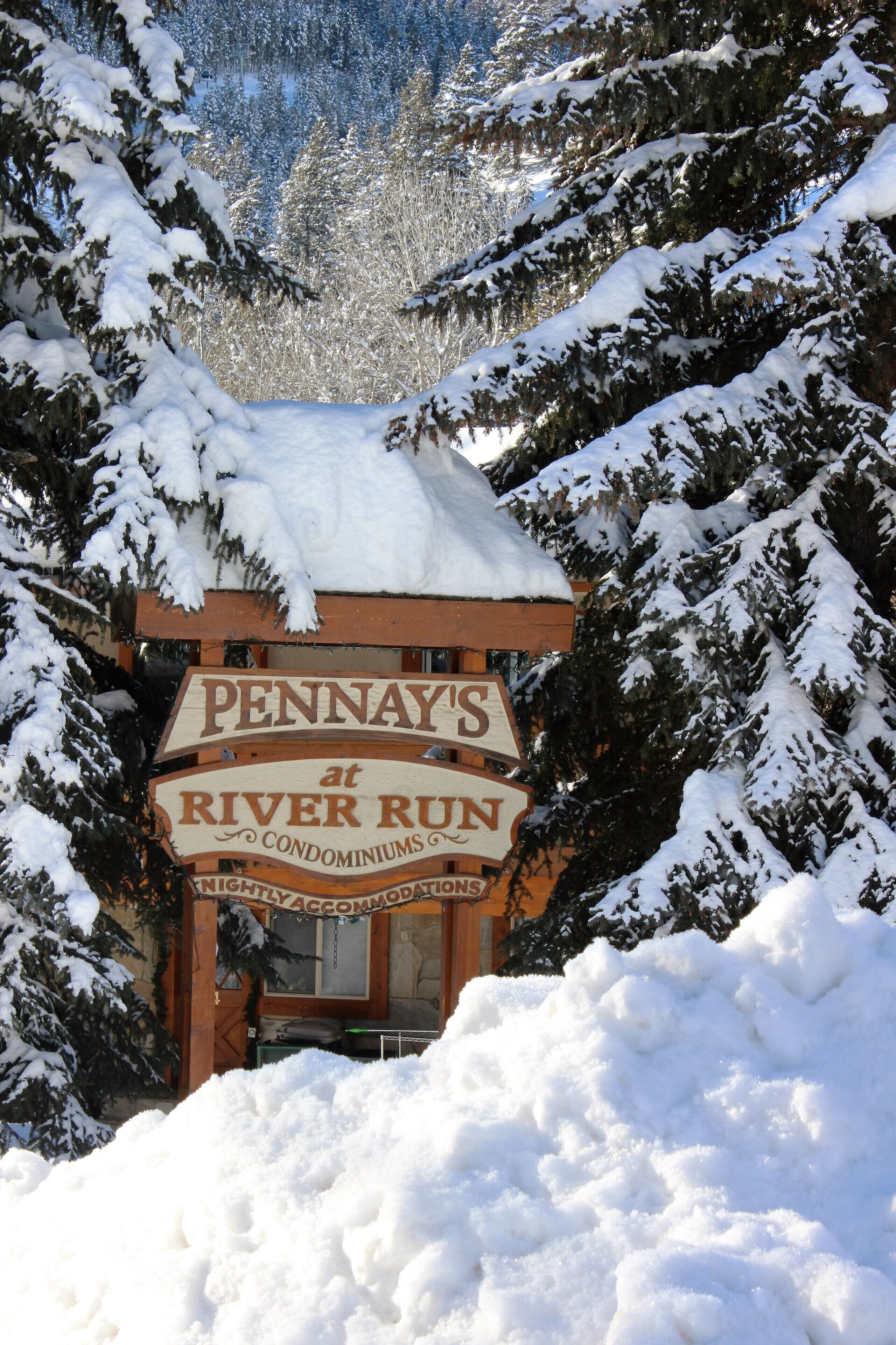 A wooden sign for Pennay's at River Run, surrounded by snow-covered trees.