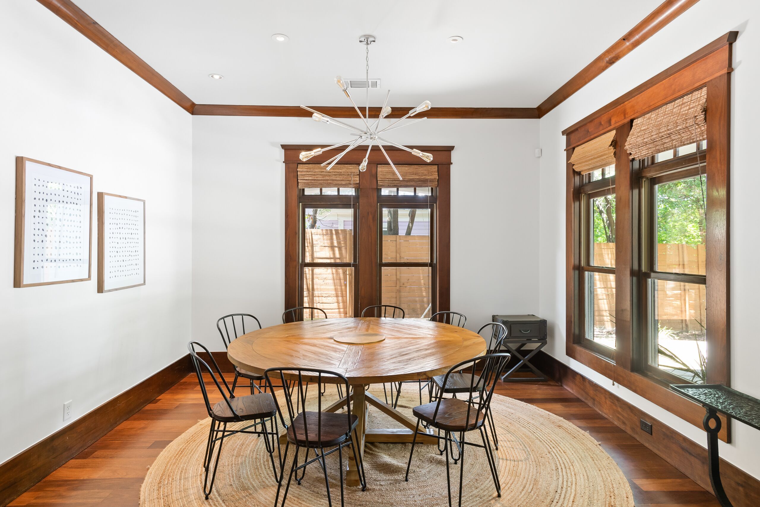 A round wooden table with eight chairs, a woven rug, and a ceiling light fixture.