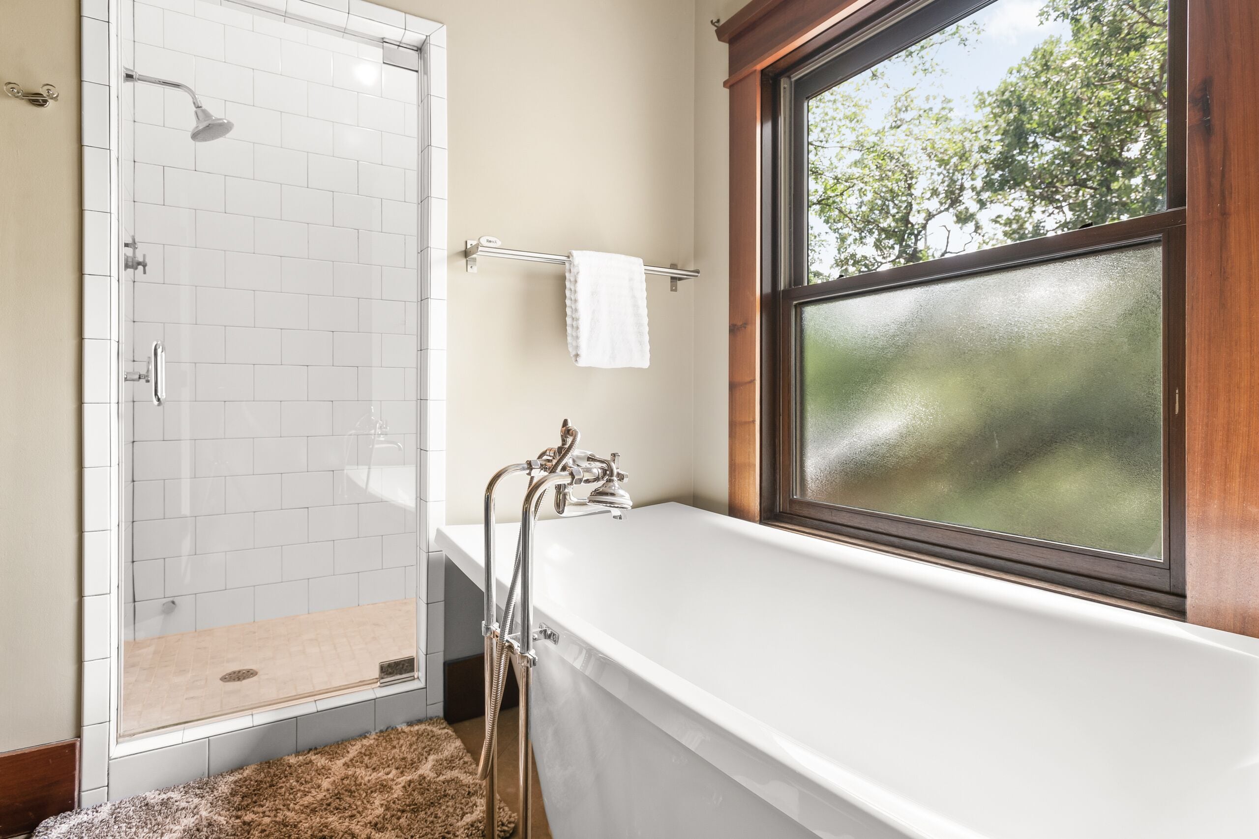 Un baño con cabina de ducha de vidrio, una bañera y una ventana con vistas a árboles.