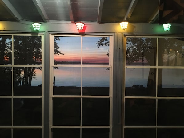 Une vue à travers une fenêtre, avec le reflet d’un coucher de soleil, un plafond en bois et un luminaire vert.