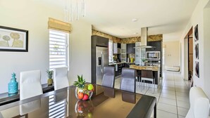 A modern kitchen with stainless steel appliances, a dining area with a glass table and white chairs, and a view of the city through the window.