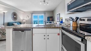 A modern kitchen with a dishwasher, oven, and microwave. There is a large window with a view of the ocean. - Cozy Beachfront Condo in Gulf Shores | Pool & Outdoor Grills | Sleeps 6 (Gulf Shores)