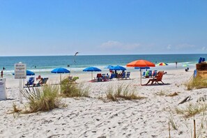 A beach with several blue and red umbrellas, lounge chairs, and a sign indicating a lifeguard on duty.