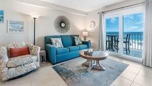 A living room with a sofa, a coffee table, and a view of the ocean through large sliding doors. - Cozy Beachfront Condo in Gulf Shores | Pool & Outdoor Grills | Sleeps 6 (Gulf Shores)