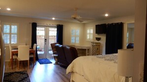Ein Schlafzimmer mit Bett, Schreibtisch, Stuhl, Deckenventilator und einem Fenster mit Vorhängen.