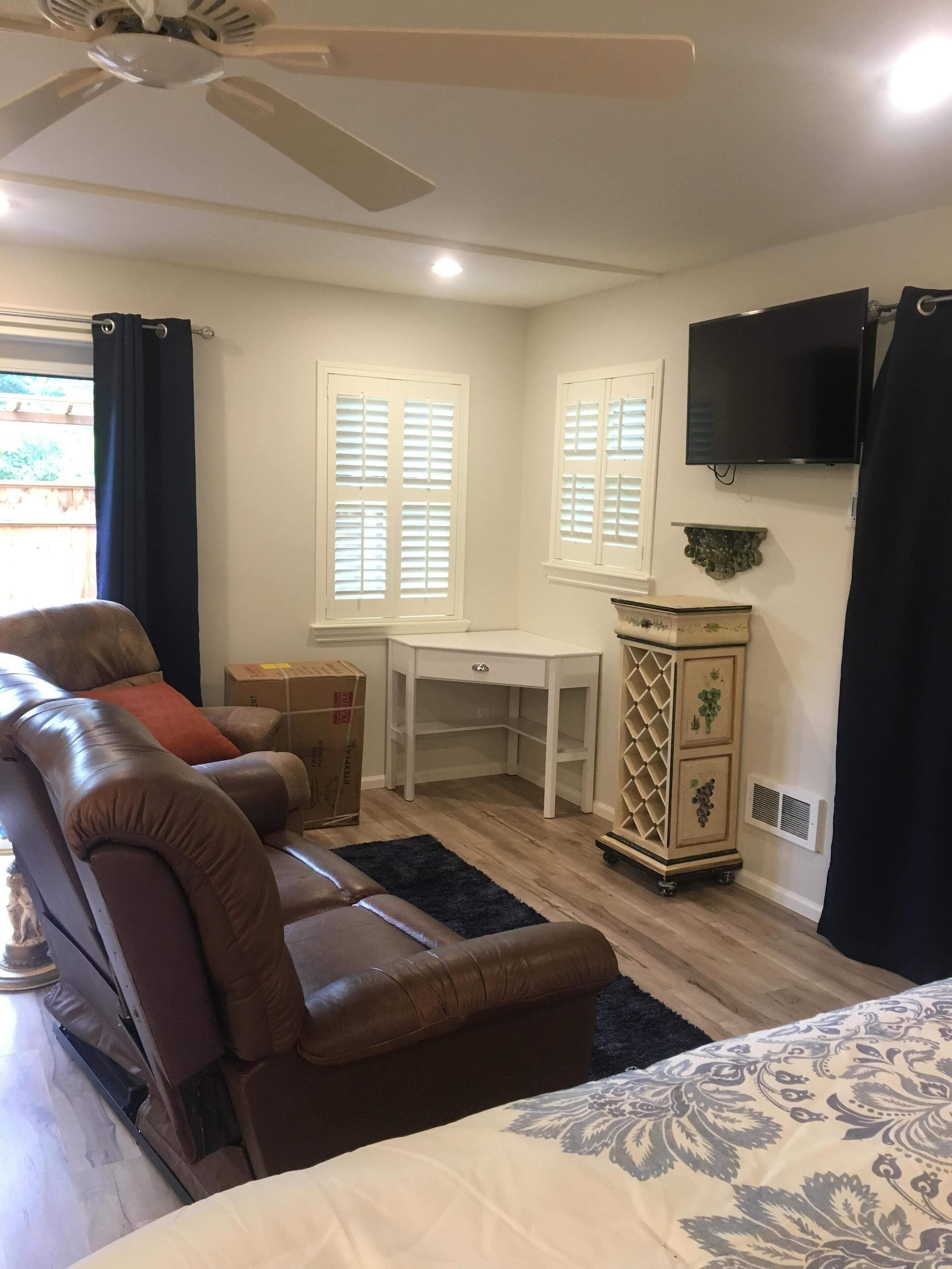 A bedroom with a bed, a desk, a chair, a television, and a window with blinds.